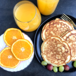 Orange juice in a glass cup, orange slices in a white plate.Pancakes in a black plate