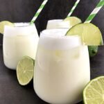 3 glasses of brazilian lemonade with halves of lime fruit around it.
